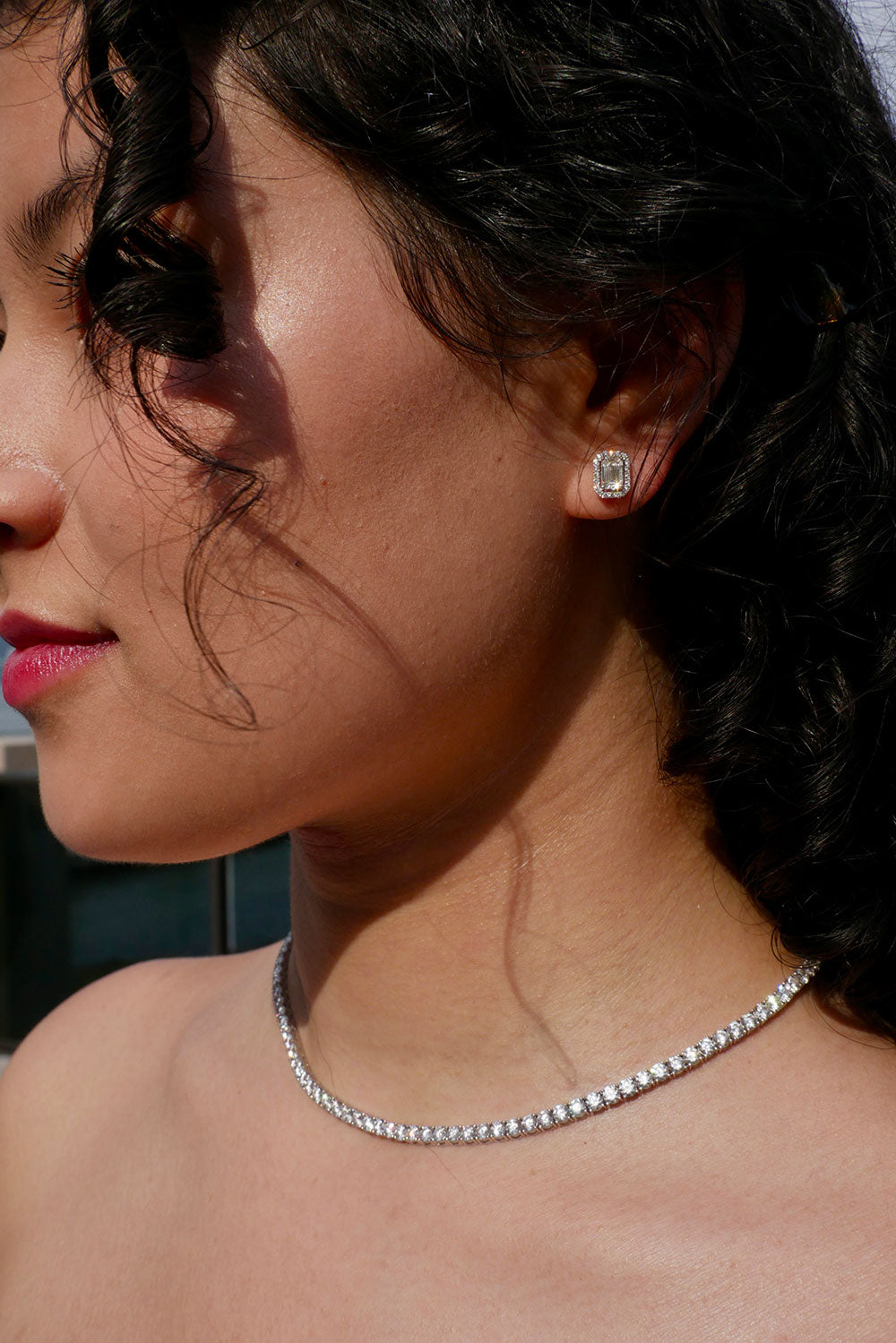 Close-up of a woman wearing a diamond earring named the headquarters and necklace.
