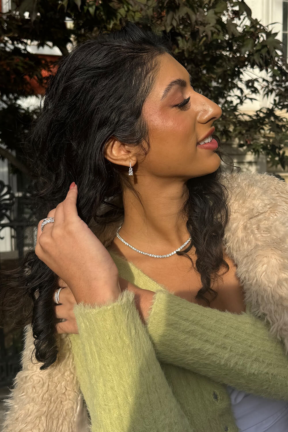 Woman wearing a green cardigan and beige fur coat with a blurred background