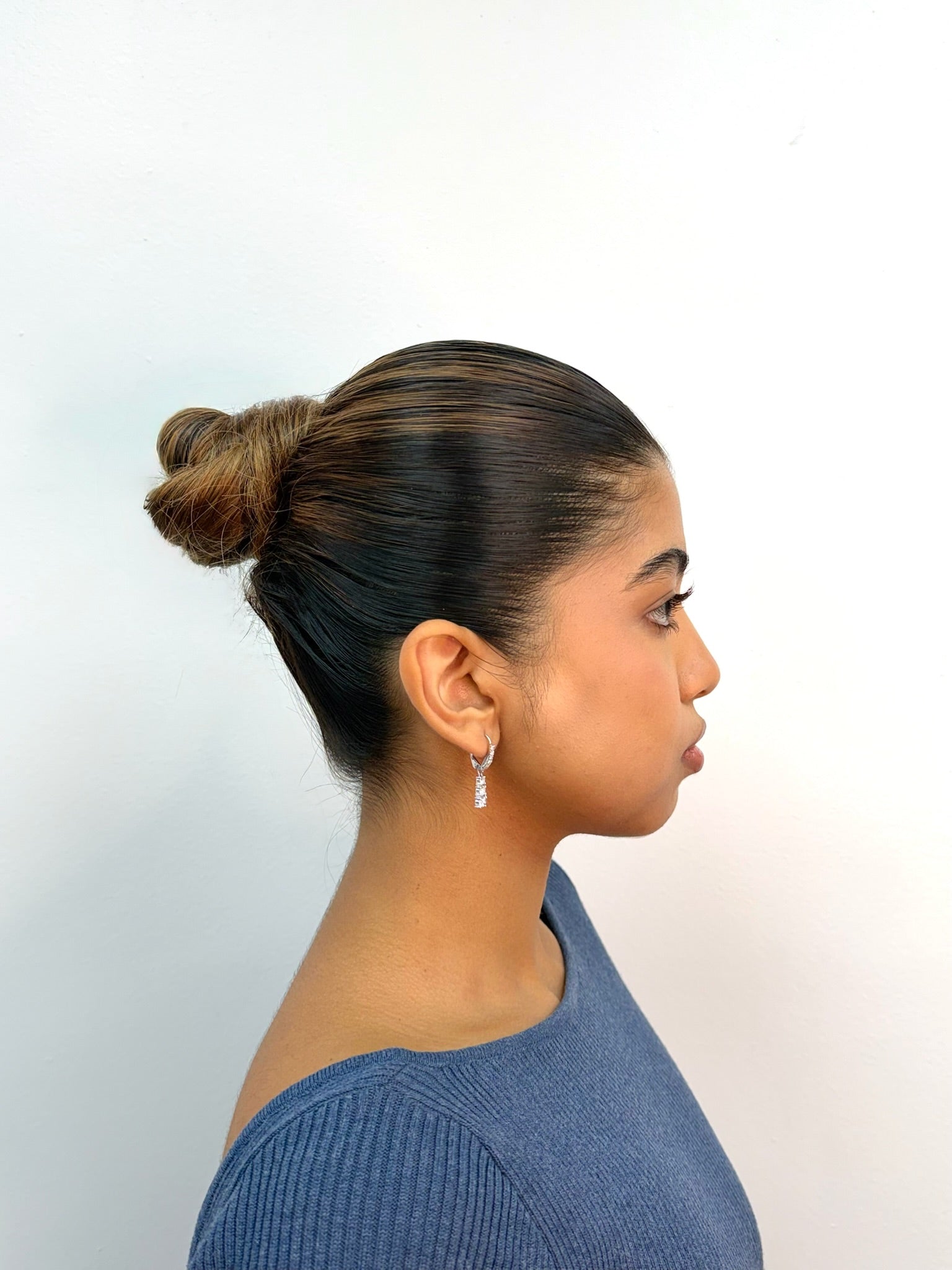 A woman in profile wearing a small silver hoop earring with a clear teardrop gemstone, shown against a plain white background.