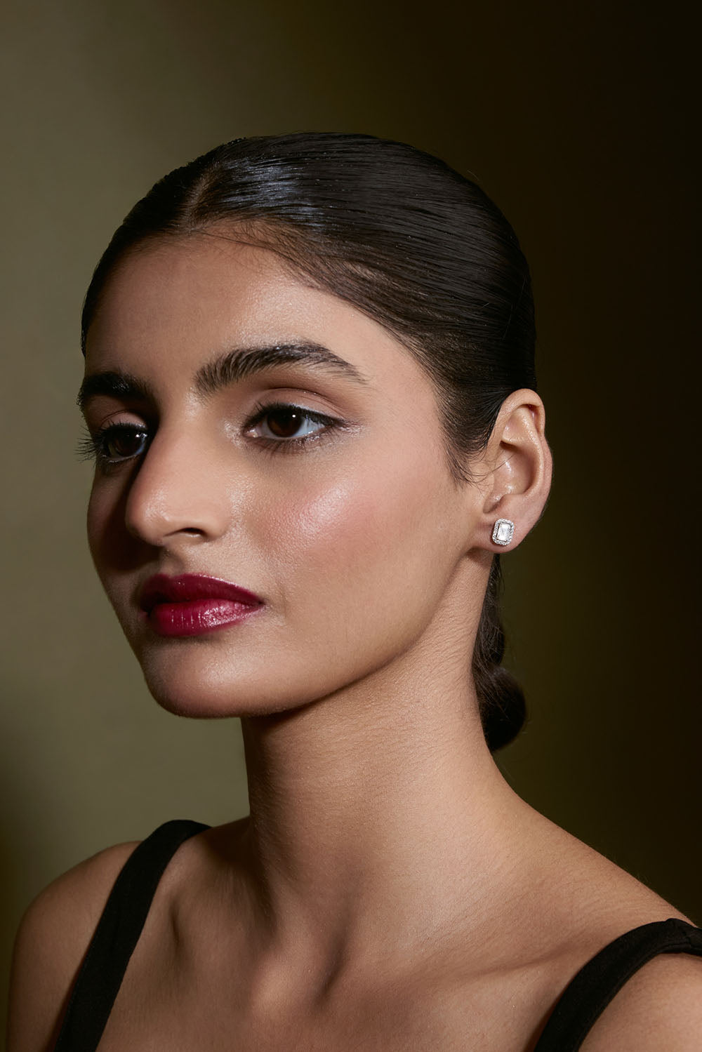 Woman with dark hair and red lipstick wearing a black top against a brown background