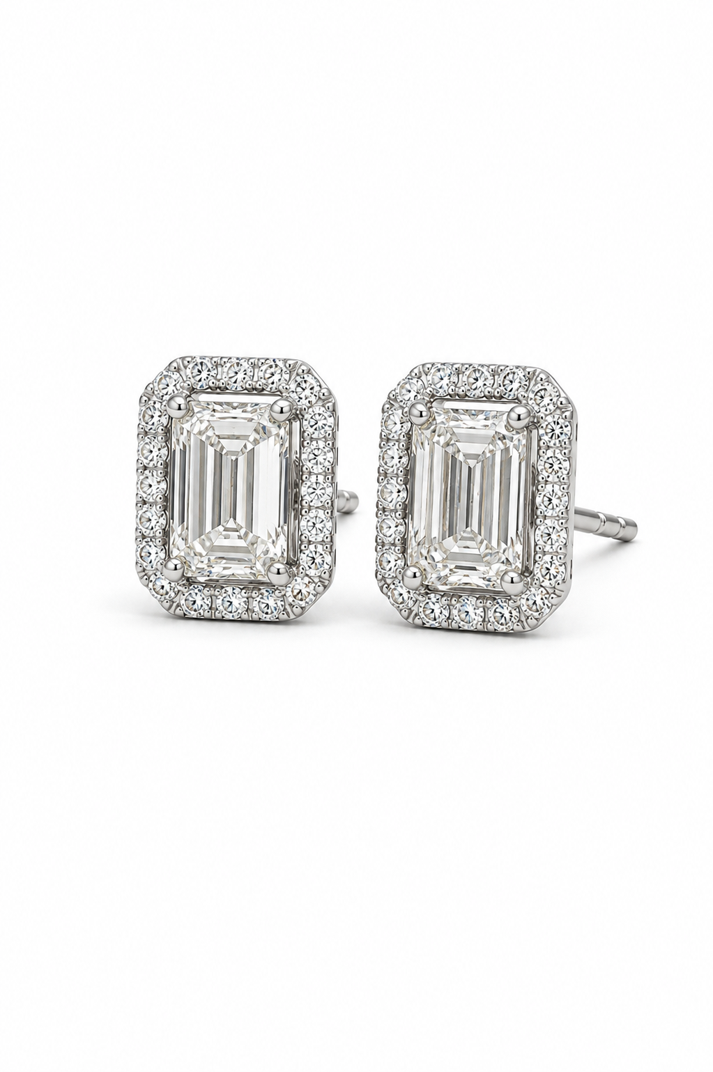 A pair of rectangular halo stud earrings featuring emerald-cut center stones surrounded by smaller clear stones in a silver-toned setting, shown on a plain white background.