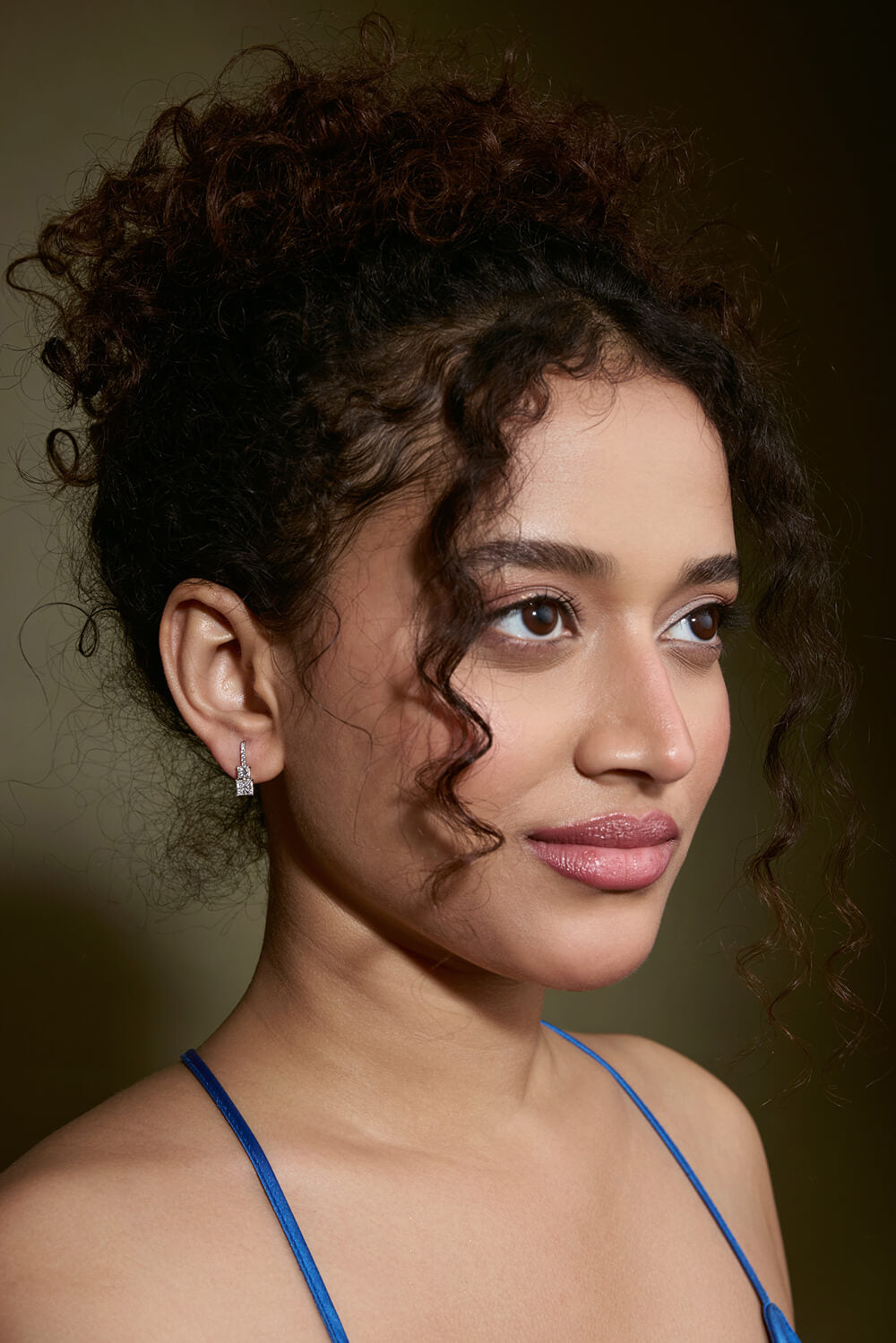 Woman with curly hair wearing a blue top against a brown background