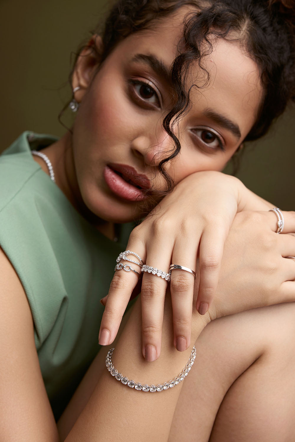 Woman wearing multiple rings and a necklace on a neutral background