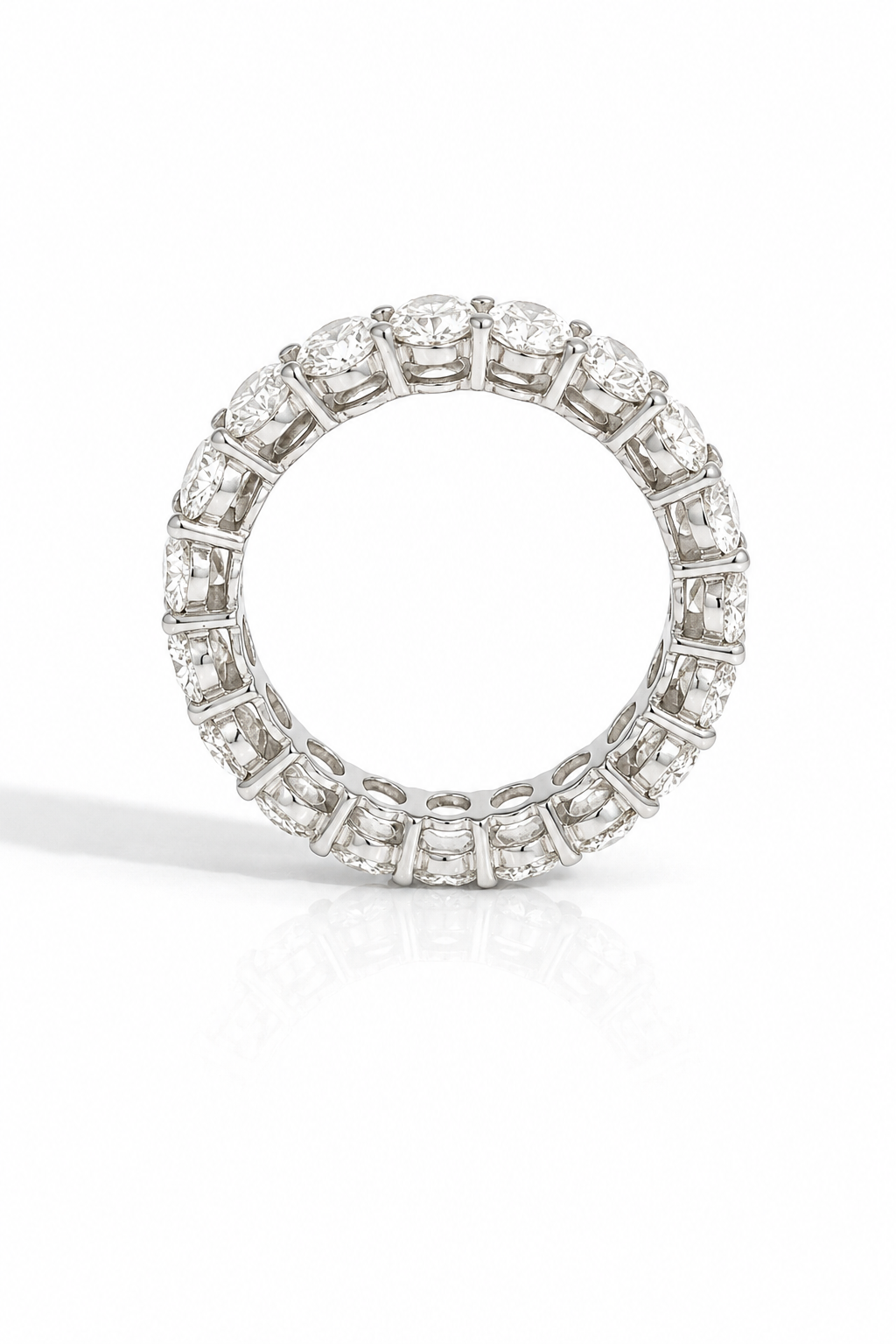 A diamond eternity ring in a silver-toned setting, photographed on a clean white background with a soft reflection underneath.