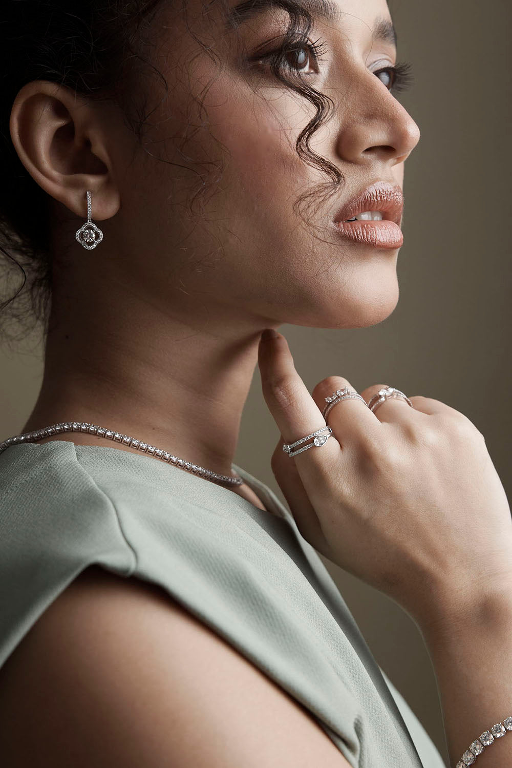 Woman wearing jewelry including earrings, rings, and a necklace against a neutral background