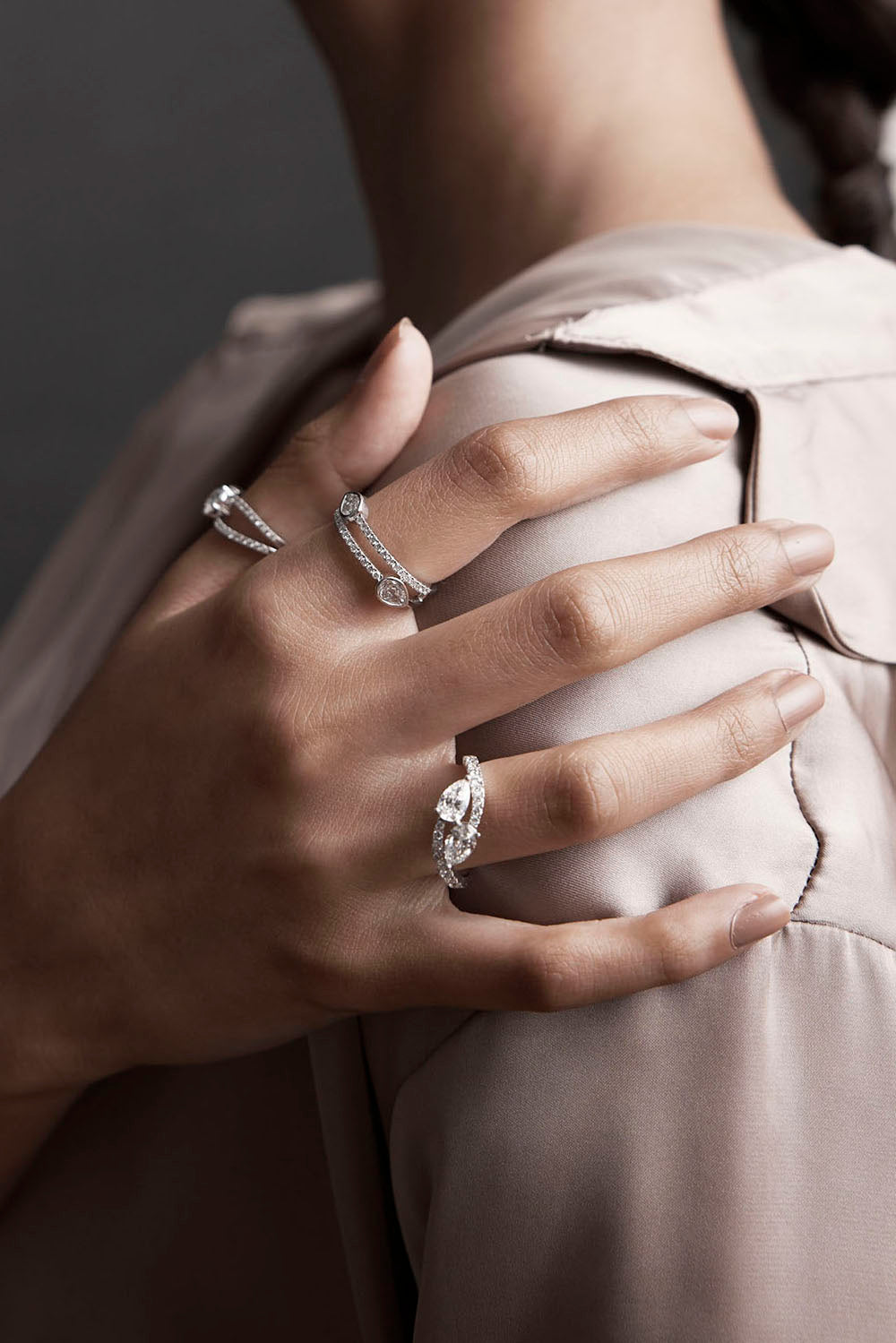 Close-up of a hand wearing multiple diamond rings on a neutral background